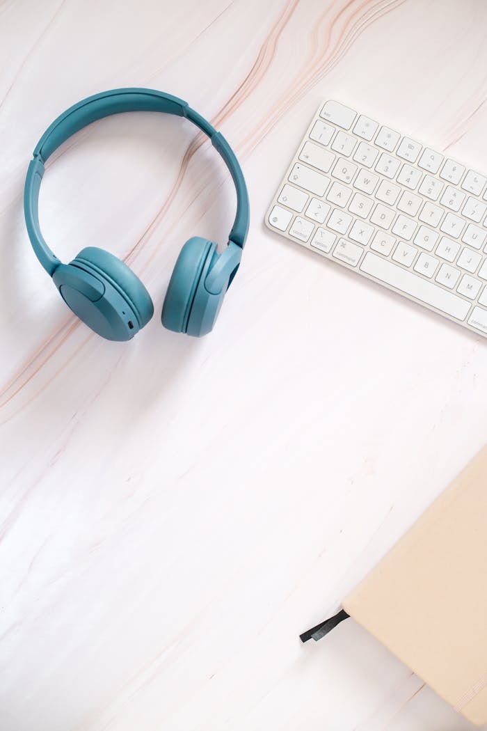 Flat lay of teal headphones, keyboard, and notebook on a desk.